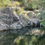 rocce di granito si specchiano sull'acqua di un fiume che forma una piscina naturale. Tutto attorno verde e vegetazione