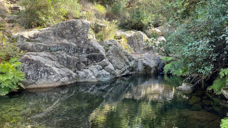 rocce di granito si specchiano sull'acqua di un fiume che forma una piscina naturale. Tutto attorno verde e vegetazione